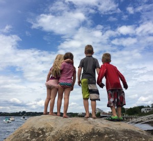 four kids from behind on a rock looking at the ocean